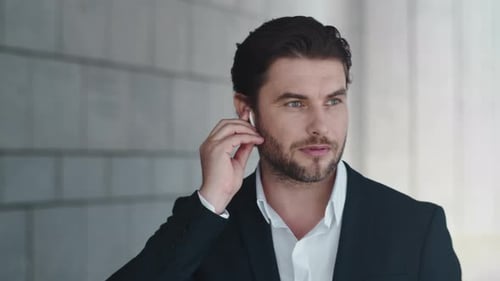 Portrait of Serious Businessman Talking by Wireless Earphones in Modern City. Closeup