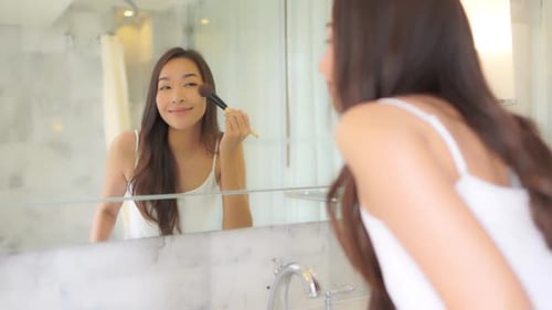 A beautiful young woman with a perfect complexion applies make-up, blush with a soft blush brush
