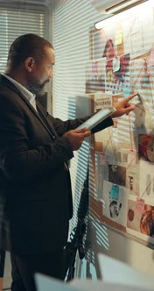 Man Examines Clues on Investigation Board in Office