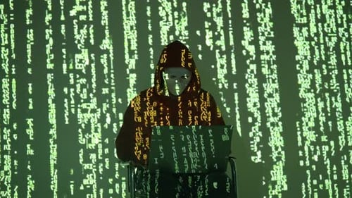 Hacker in Hoodie and Mask Working on Laptop Surrounded by Falling Green Code on Dark Wall