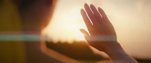 Woman Holding Hand Up to Setting Sun