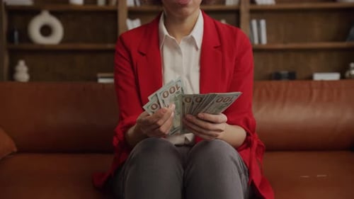 Woman Counting One Hundred Dollar Bills on Couch