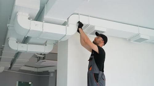 Tradesman Repairing Ventilation System in White Room