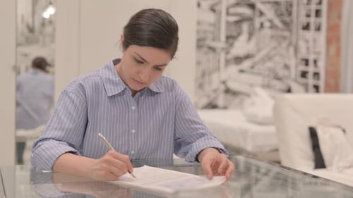 Woman Writing on Document at Glass Table Indoors
