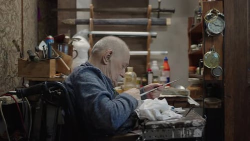 Senior Gray Haired Male Master in a Wheelchair Working at His Workshop Sharpening Japanese Swords