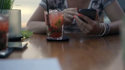 Woman's hands using smartphone at cafe table with cocktail in casual lifestyle