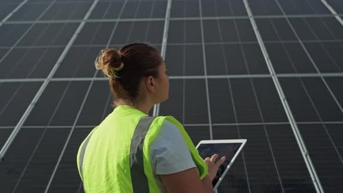 Female Engineer Adjusts Solar Panels on Tablet