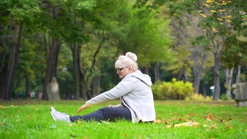Portrait senior retired woman exercising on a mat on lawn a park Old female does yoga practice lotus