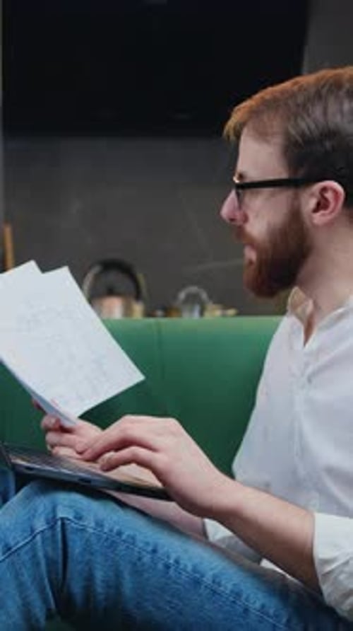 Adult Man Working in Kitchen Sitting on Sofa with Laptop Browsing Documents Freelancer Work on Home