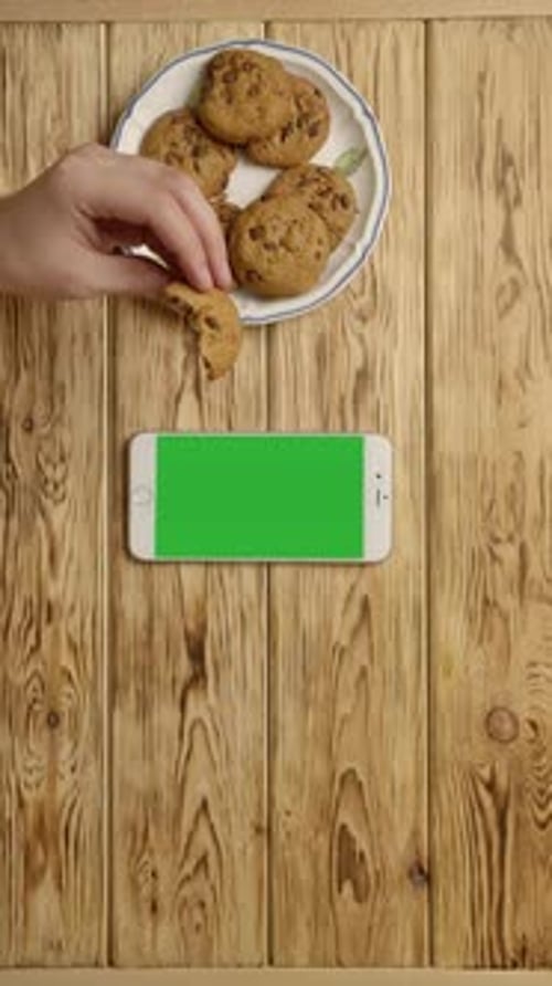 Vertical of Unrecognizable Person Drinking Coffee and Eating Cookies Near Smartphone
