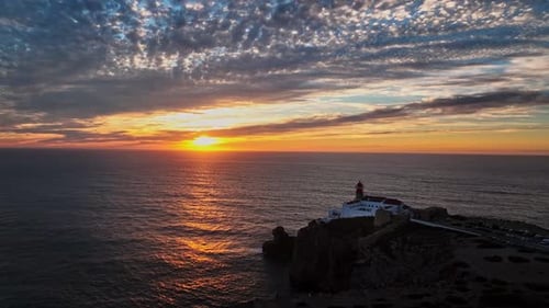 Luftaufnahme, die den Leuchtturm vor dem weiten offenen Meer bei Sonnenuntergang zeigt.