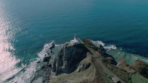 Panoramaaufnahme des weißen Leuchtturms auf der felsigen Klippe am Meer. Wellen stürzen auf den
