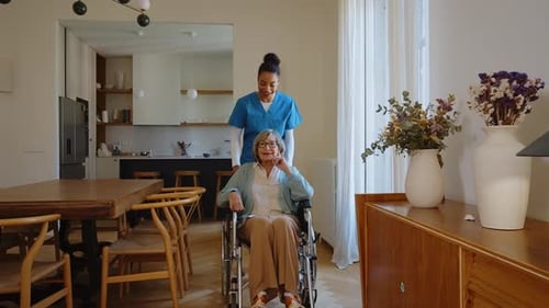 Caregiver Pushing Senior Woman in Wheelchair Indoors