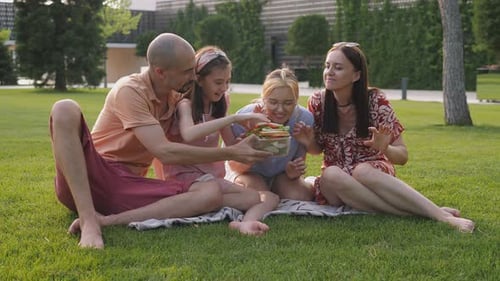 A Family is Eating Fresh Sandwiches Together in the Park Sitting on the Grass