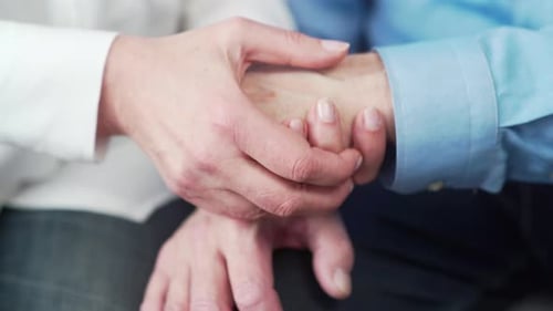 close up older elderly people hands. Old man holds a woman hand sitting together at home indoor.