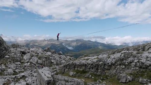 Crazy Person balancing on Slackline on top of mountain peal during summer - Aerial approaching and r