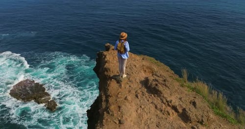Woman in Hat Enjoying of Ocean Woman Standing Up High on a Cliff Edge Rear View Happy Traveler