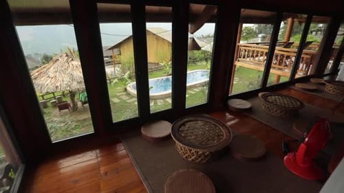 A cozy cabin view of a pool and garden through large windows on a rainy day