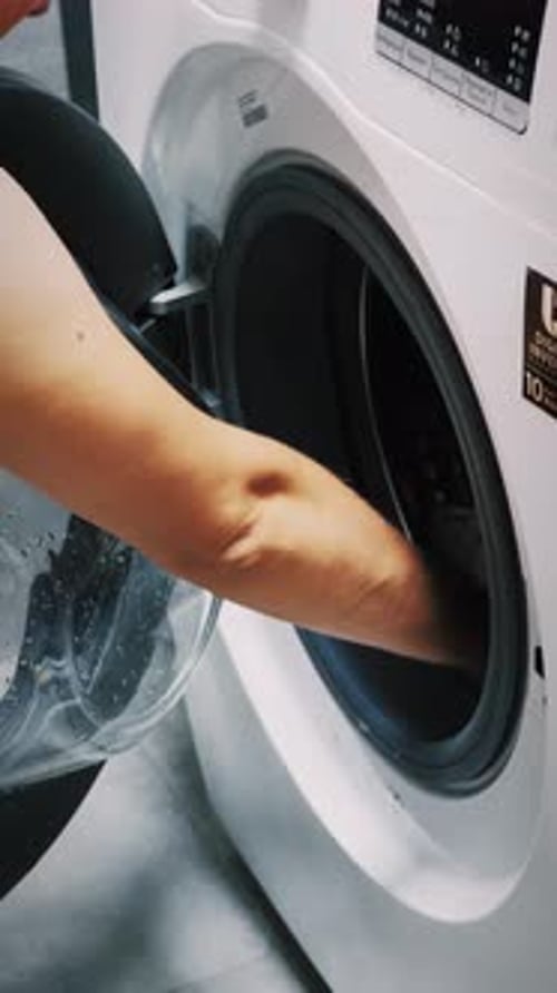 Frau holt saubere Wäsche aus der Waschmaschine, Nahaufnahme. Vertikales Video