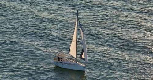 Establishing Aerial Shot of a White Yacht with Black Sails in the Rays of the Setting Sun Glare on