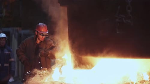 Industrial worker tending to molten metal in factory