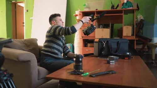 Man Reaches for Camera Gear in Home Studio Organizing Equipment on Wooden Table
