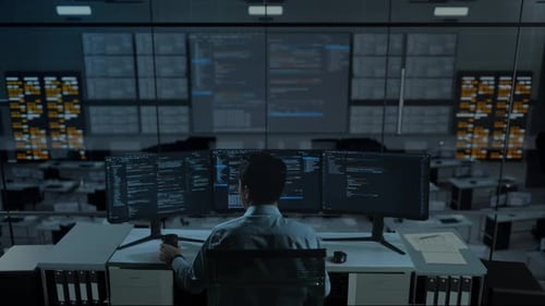 Asiatischer Mann trinkt Kaffee und benutzt Computer, um Code mit mehreren Bildschirmen im Büro zu schreiben