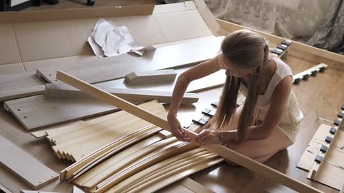 Une jeune jolie fille caucasienne assemble un nouveau lit en bois dans le salon