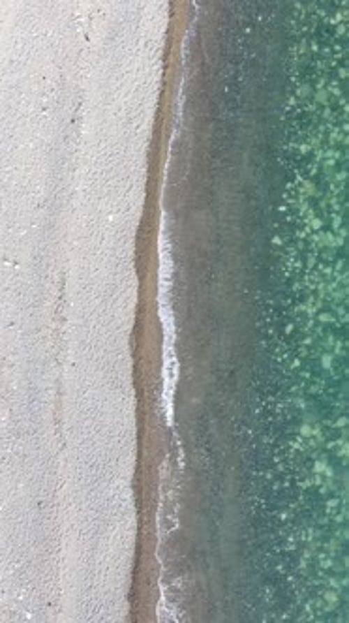 Aerial Vertical View of Beach with Wave Caressing Shore Sun Glare Small Waves on the Water Surface