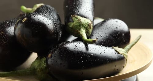 Fresh wet eggplants turning on light table against grey background, closeup