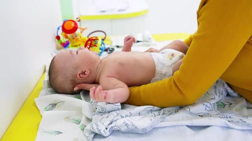 Mother is taking baby and puts him on the clothes. Baby in diaper is looking up. Side view.