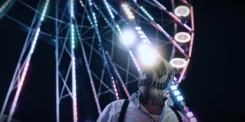 Masked Figure in Front of Ferris Wheel at Night