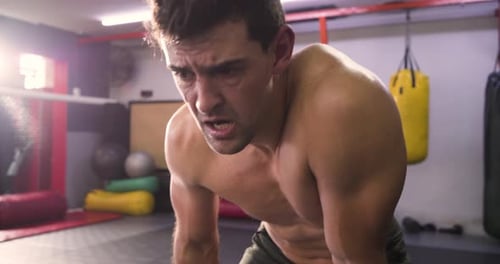 Male boxer recovering after training, breathing heavily at gym, removing mouthguard, wiping sweat