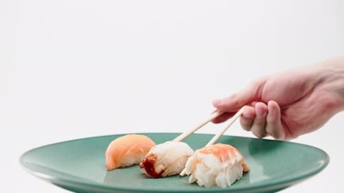 Close-up of a male hand using chopsticks to take one eel sushi from a plate of salmon and sushi