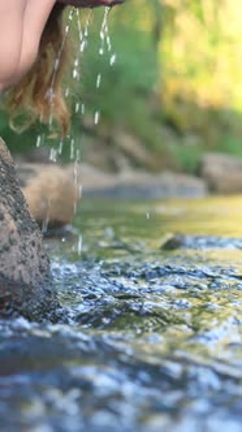 Young Woman Drinking Fresh Water From a Clean Forest Stream