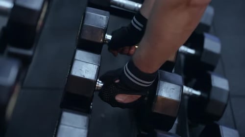 Man hands taking dumbbells from shelf at the gym - close up