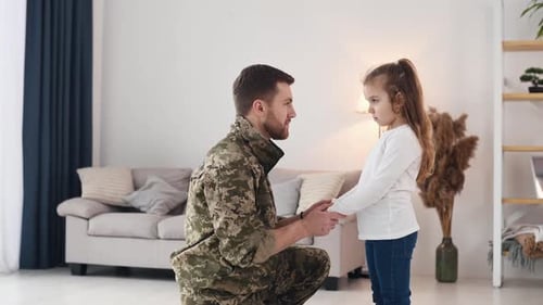 Side view. Holding by the hands. Soldier in uniform is at home with his little daughter