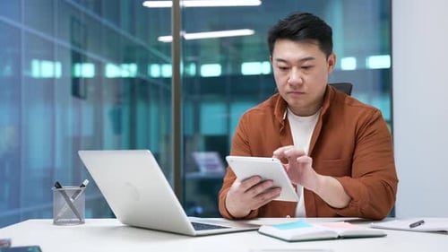Asian businessman is using digital tablet sitting at desk at workplace in business office. Manager
