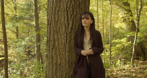 Black-Haired White Girl Leaning Against Oak Tree Trunk, In A Ravine With Afternoon Dappled Sunlight