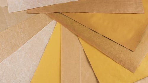 Rotating sheets of handmade craft paper in natural shades of beige, ochre and sand create a textured