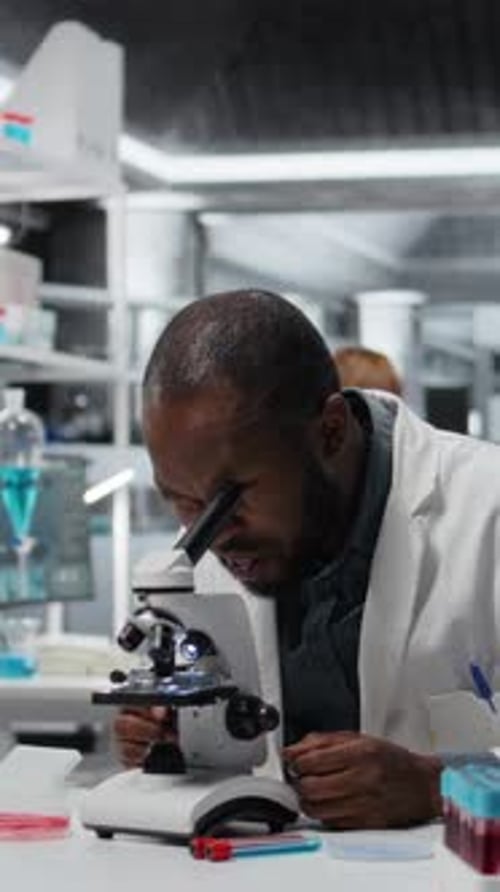 Man in Lab Coat Uses Microscope in Lab