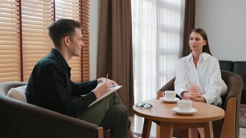 Man Taking Notes While Woman Talks in Office