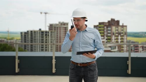 Engenheiro de construção usando walkietalkie e tablet no telhado