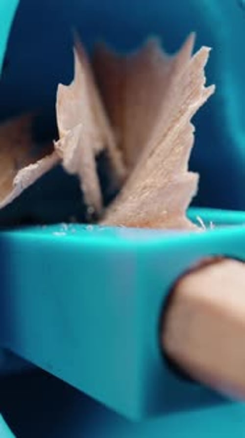 Vertical video. A wooden pencil is sharpened in a blue plastic sharpener, close-up.