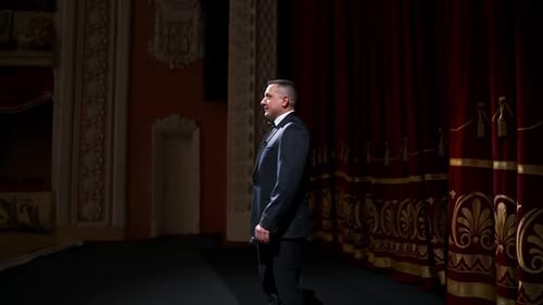 Actor steps on classic theater stage. Man in suit is walking in spotlights during the performance.