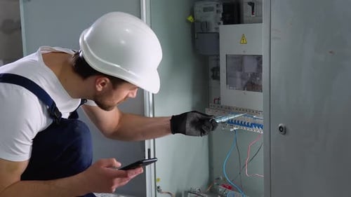 Electrician Works on Electrical Panel with Smartphone