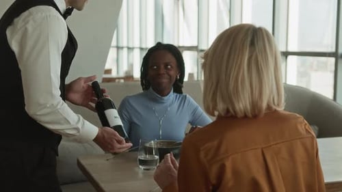 Server Presenting Bottle of Wine to Diverse Female Guests in Modern Restaurant