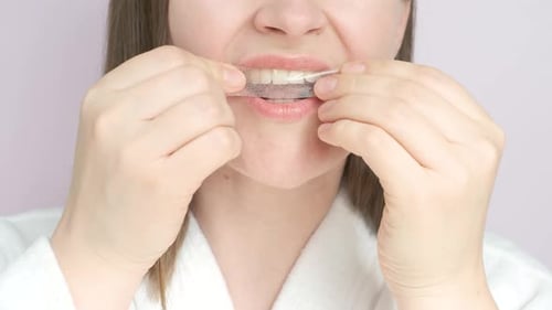 Portrait of young woman holding a whitening strip for teeth, close-up.