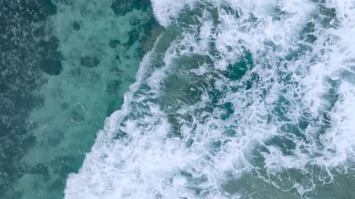 Top Down Slow Motion Drone View of turquoise clear water and crashing waves over shallow coral reef