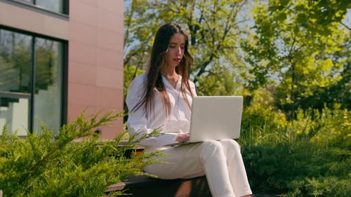 Woman Working Outdoors on Laptop in Suburban Setting